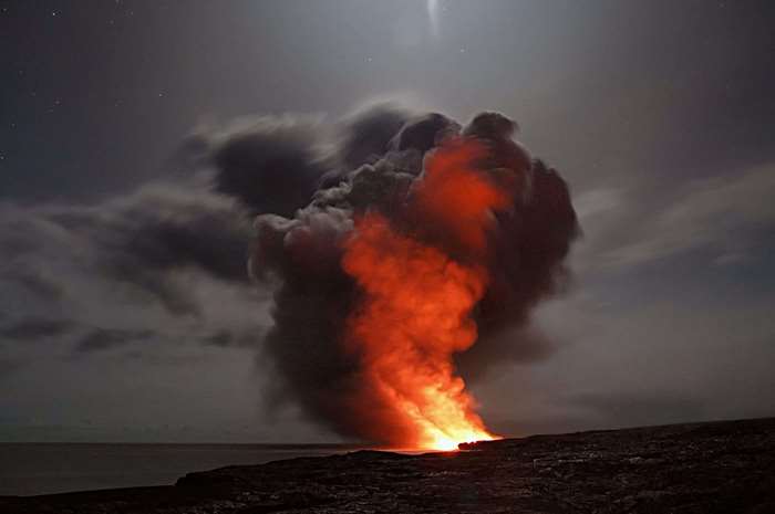 Volcano erupting with lava and smoke at night