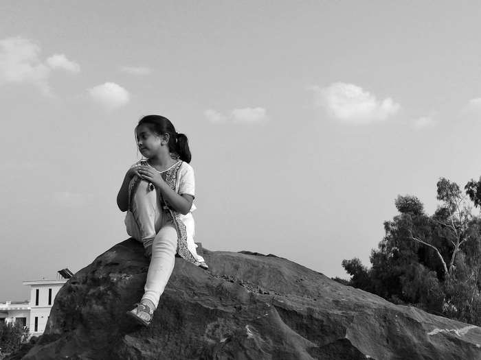 Girl sitting on a rock with trees and clouds