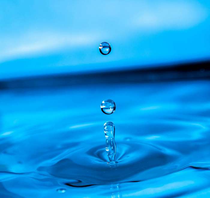 Water drops falling into blue water with ripples