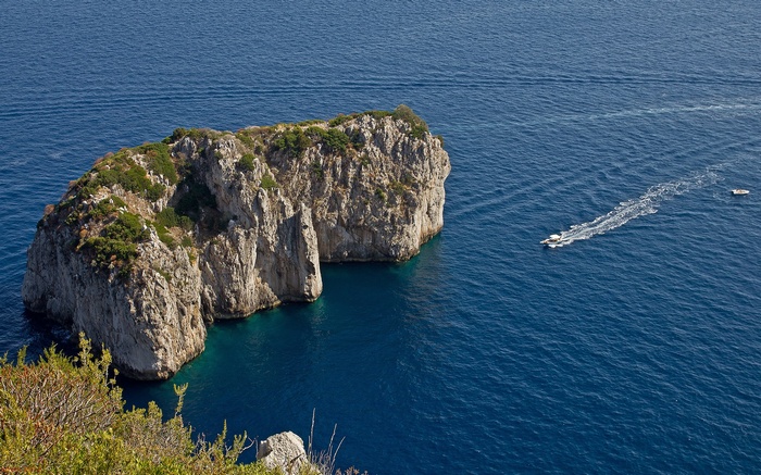 Rocky island with boats in blue sea
