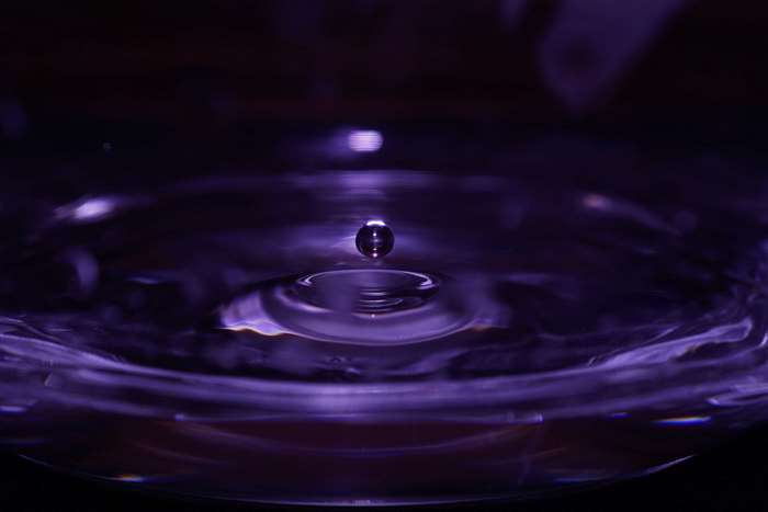 Water drop falling into purple liquid creating ripples