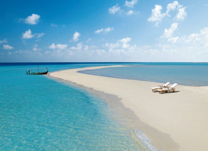 Maldives beach with a boat and lounge chairs