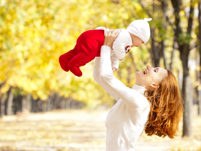 Mother holding baby in park during fall