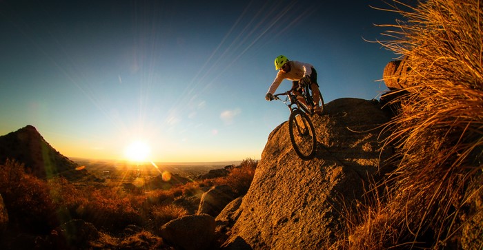 Mountain biker riding down a rocky slope at sunset