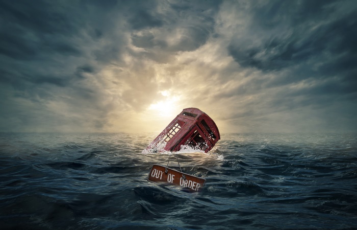 Red telephone booth sinking in the sea with 'Out of Order' sign