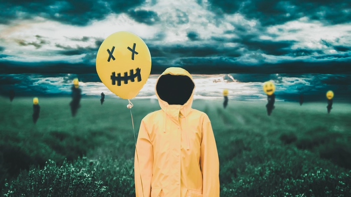 Person in yellow raincoat holding a balloon with a face
