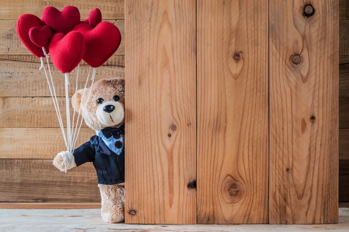 Teddy bear with heart balloons behind wooden planks