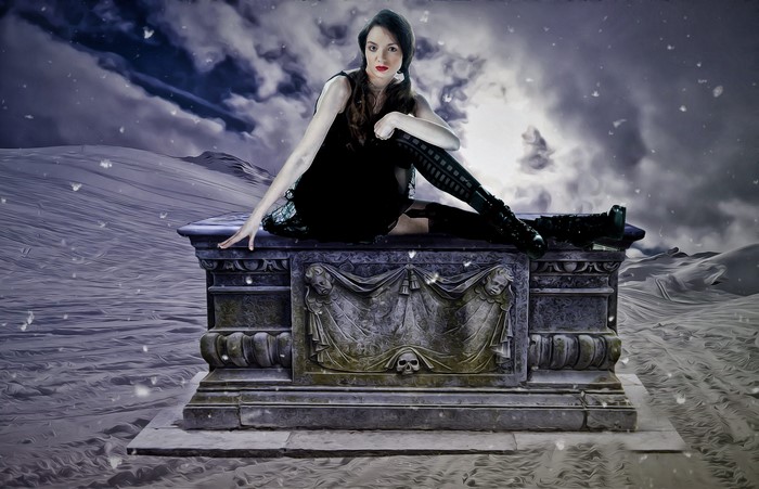 Gothic woman sitting on a tombstone in a snowy landscape