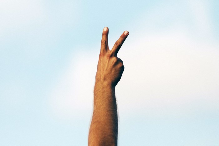 Hand making peace sign against blue sky