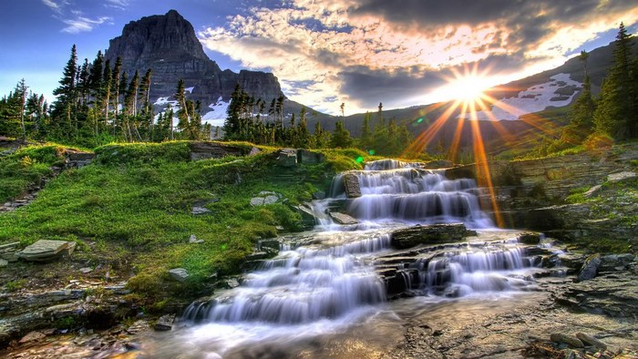 Waterfall cascading down rocks with mountain and sun