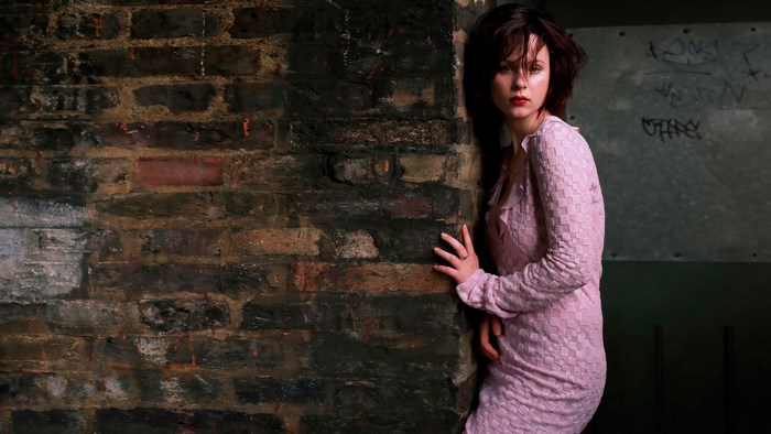 Thora Birch leaning against a brick wall