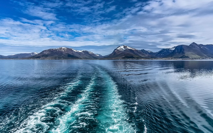 Wake from a boat in front of snow-capped mountains