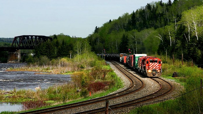 Train on tracks by a river and forest