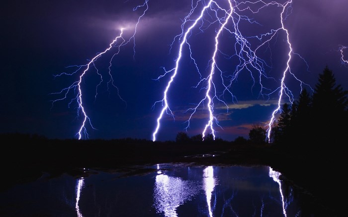Lightning strikes over a dark landscape and water