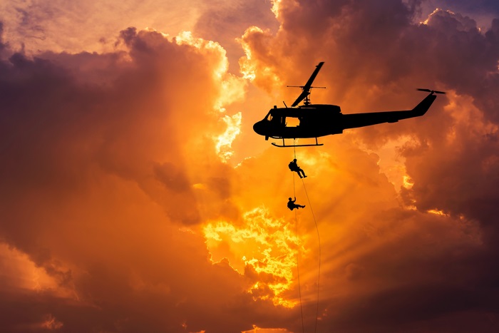 Helicopter rappelling soldiers during sunset