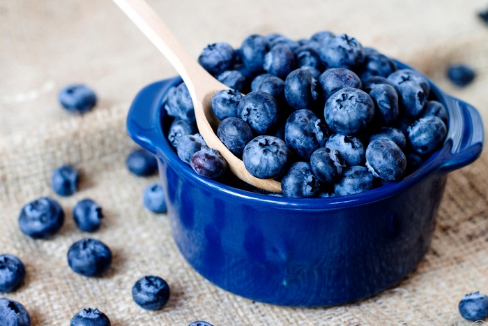 Blueberries in a blue bowl with a wooden spoon