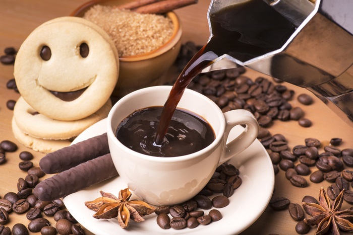Coffee being poured into a cup with cookies and coffee beans