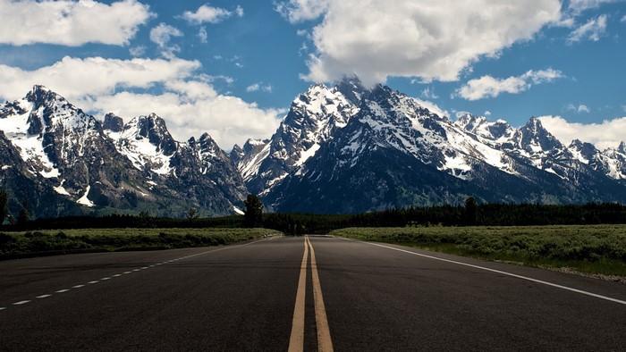 Road leading to snow-capped mountains under a cloudy sky