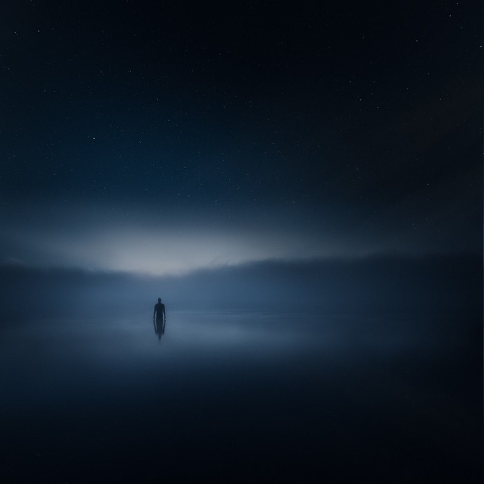Man standing in water under starry night sky with mist