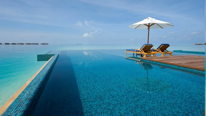 Infinity pool overlooking tropical ocean with lounge chairs