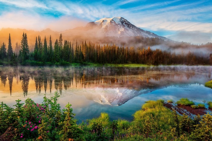 Mount Rainier reflected in a misty lake with pine trees