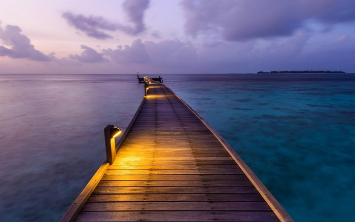 Wooden pier with lights over calm sea at sunset