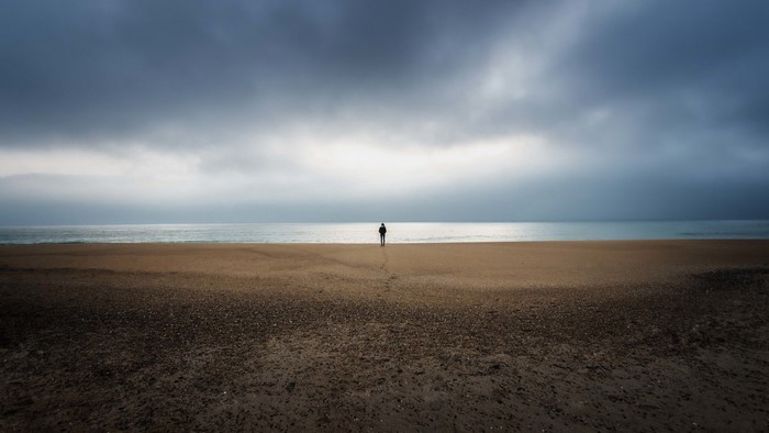 Person standing on a beach with stormy clouds