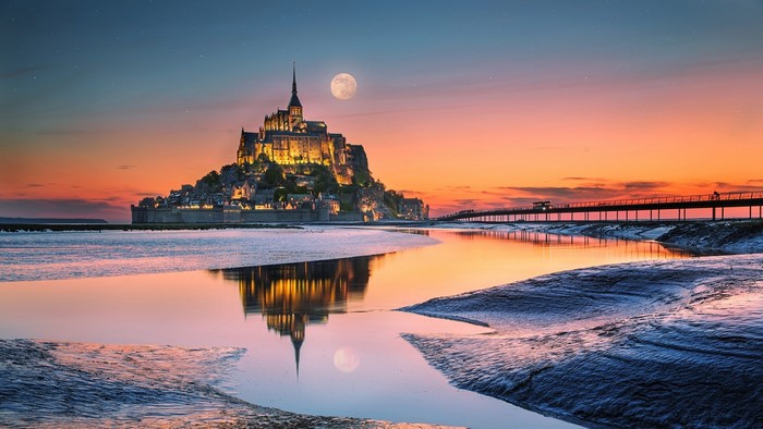 Mont Saint-Michel monastery at sunset with moon and reflection