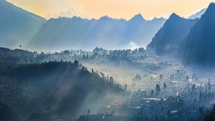 Misty valley with sun rays over mountains and village