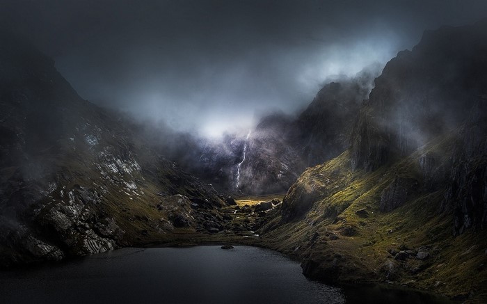 Misty mountain valley with a waterfall and lake