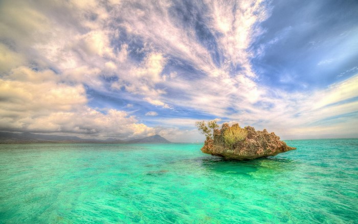 Rock island in turquoise water under cloudy sky