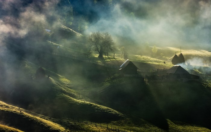 Misty mountain village with haystacks and houses at sunrise