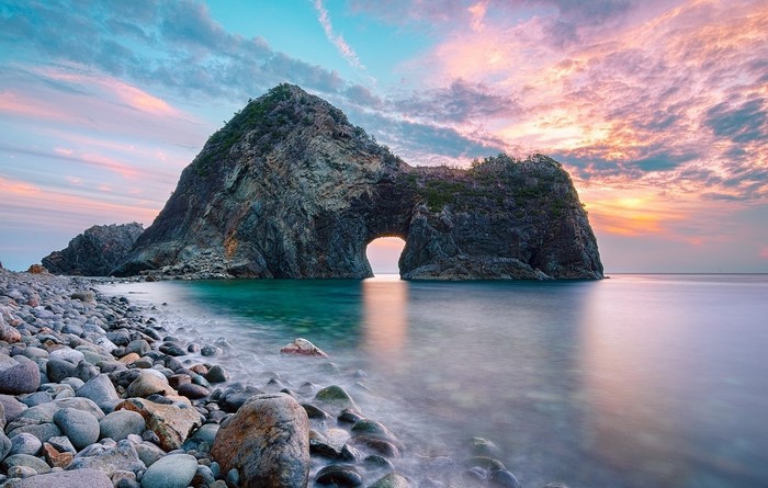 Rock arch gate on a beach at sunset
