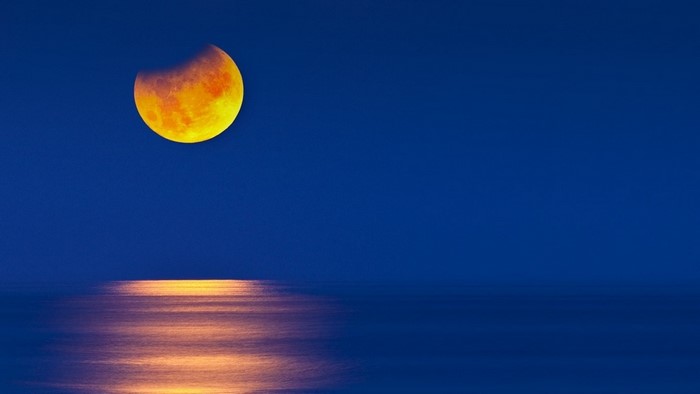 Lunar eclipse over the ocean at night