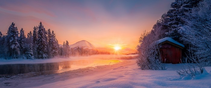 Winter sunrise over a snowy landscape with a cabin