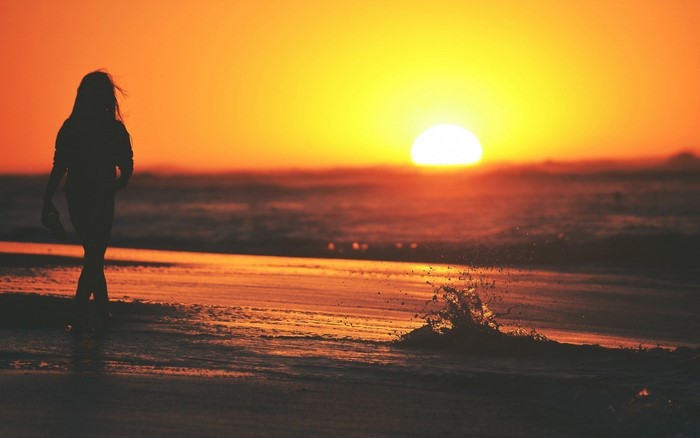 Silhouette of a woman walking on a beach at sunset