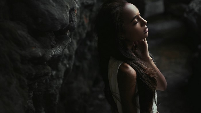 Woman with long hair touching her neck near rocks