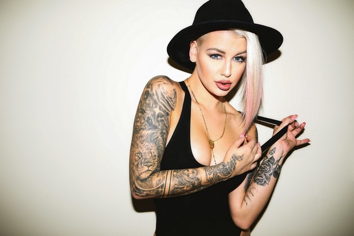 Woman with blonde hair and tattoos wearing a hat
