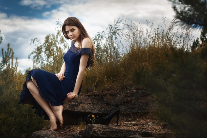 Woman in blue dress sitting on rocks in nature