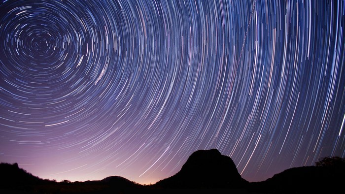 Star trails over silhouetted mountains at night
