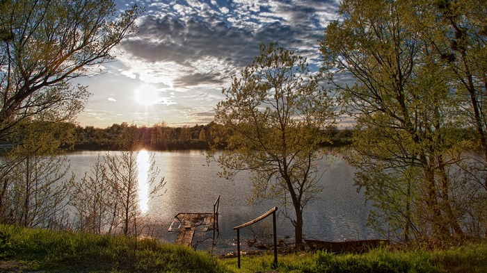Sunset over a calm lake with trees and a small dock