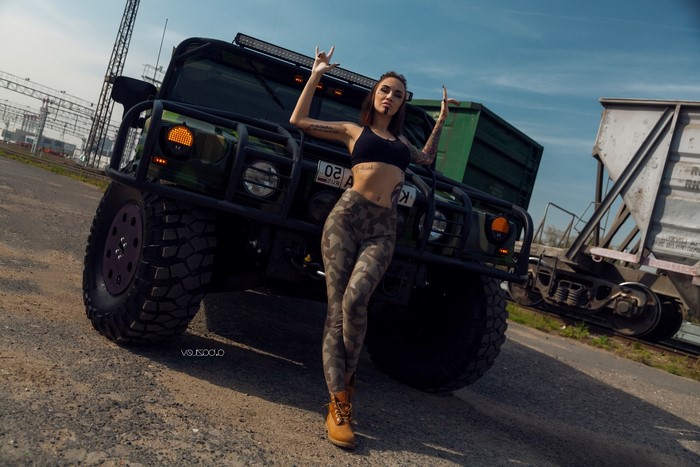 Woman with tattoos posing by a Hummer and train cars