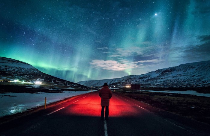 Person walking on road under Aurora Borealis