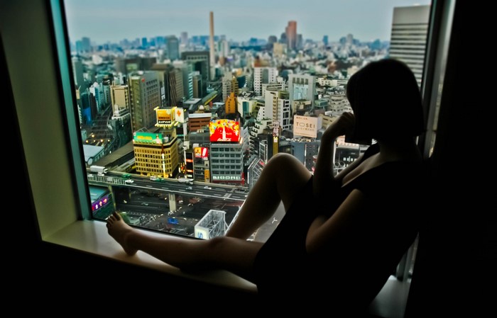 Woman silhouetted on window sill overlooking Tokyo cityscape