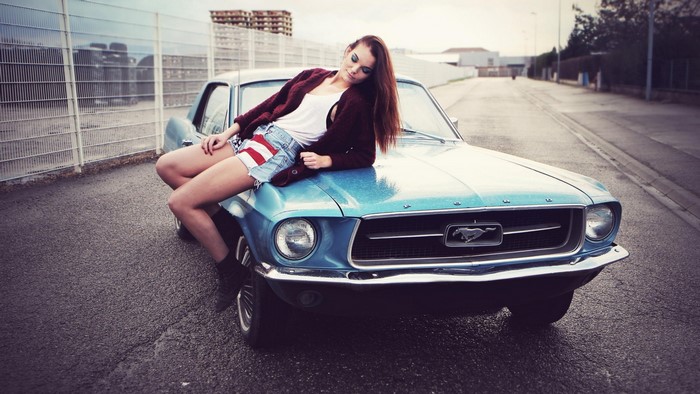 Woman in denim shorts posing on a blue Ford Mustang