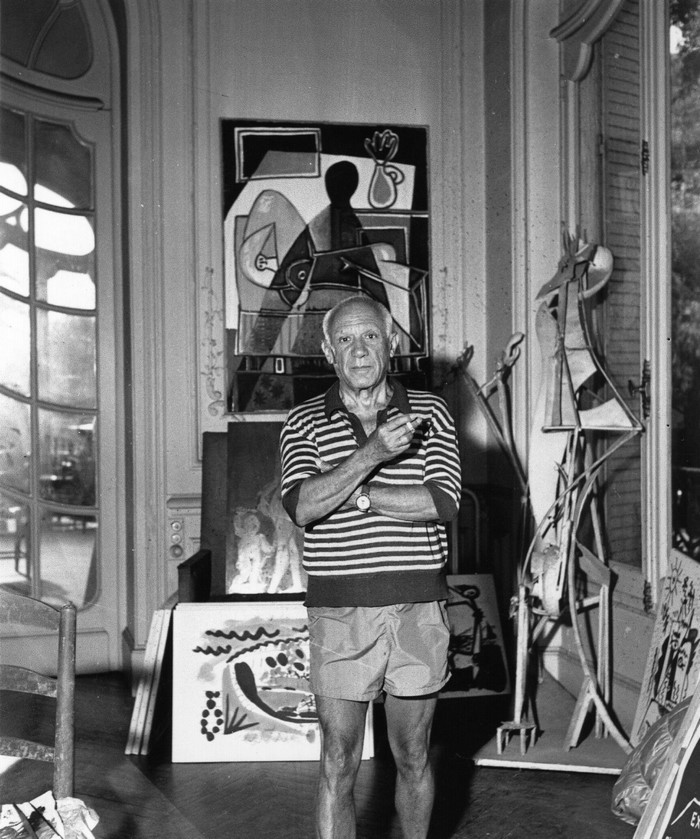 Pablo Picasso in his studio with paintings