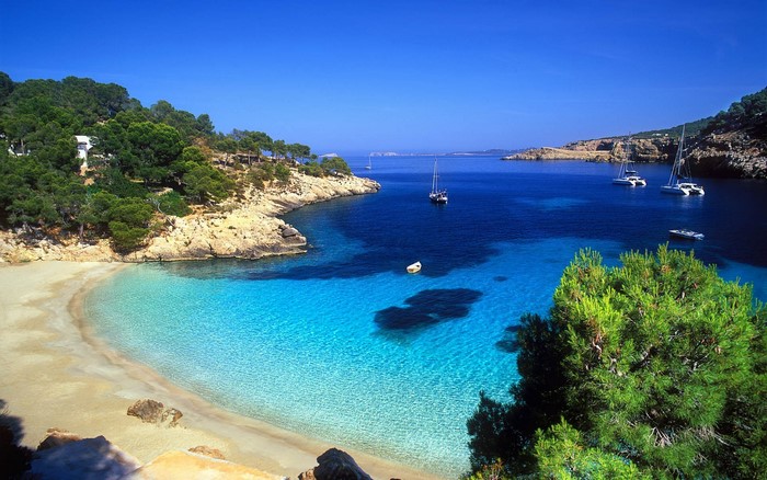 Beautiful beach with clear blue water and sailboats