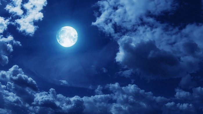 Full moon shining through dark clouds at night