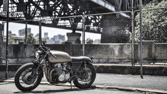 Honda motorcycle parked near a chain-link fence and bridge