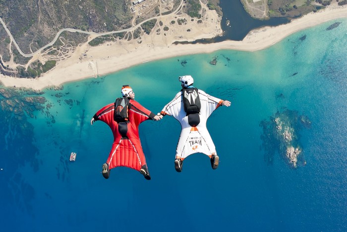 Two skydivers in wingsuits over a beach and sea